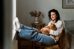 Woman sitting with cat, smiling. Pets are taking care of our health in many ways.